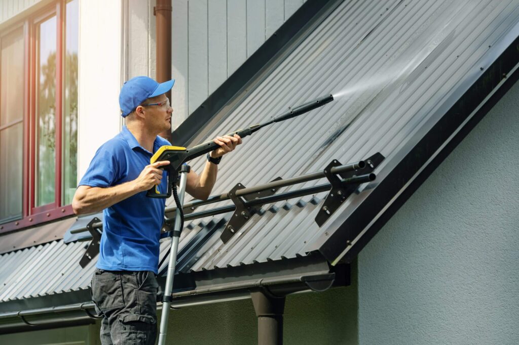 Technician using soft washing technique to clean a metal roof, showcasing professional house washing services for enhanced curb appeal and maintenance.