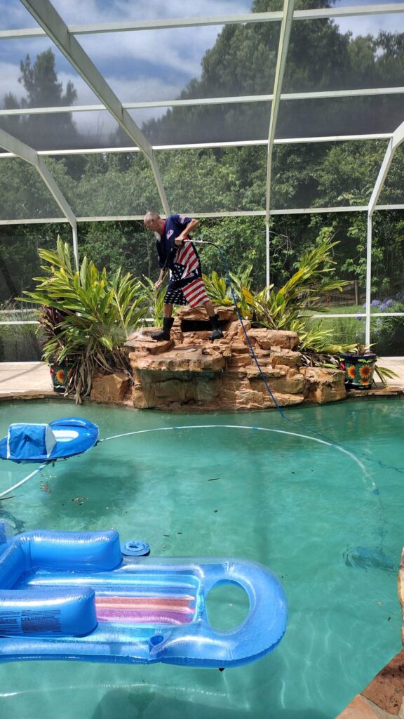 A-man-wearing-shorts-with-an-American-flag-pattern-boots-and-a-shirt-is-standing-on-a-faux-rock-waterfall