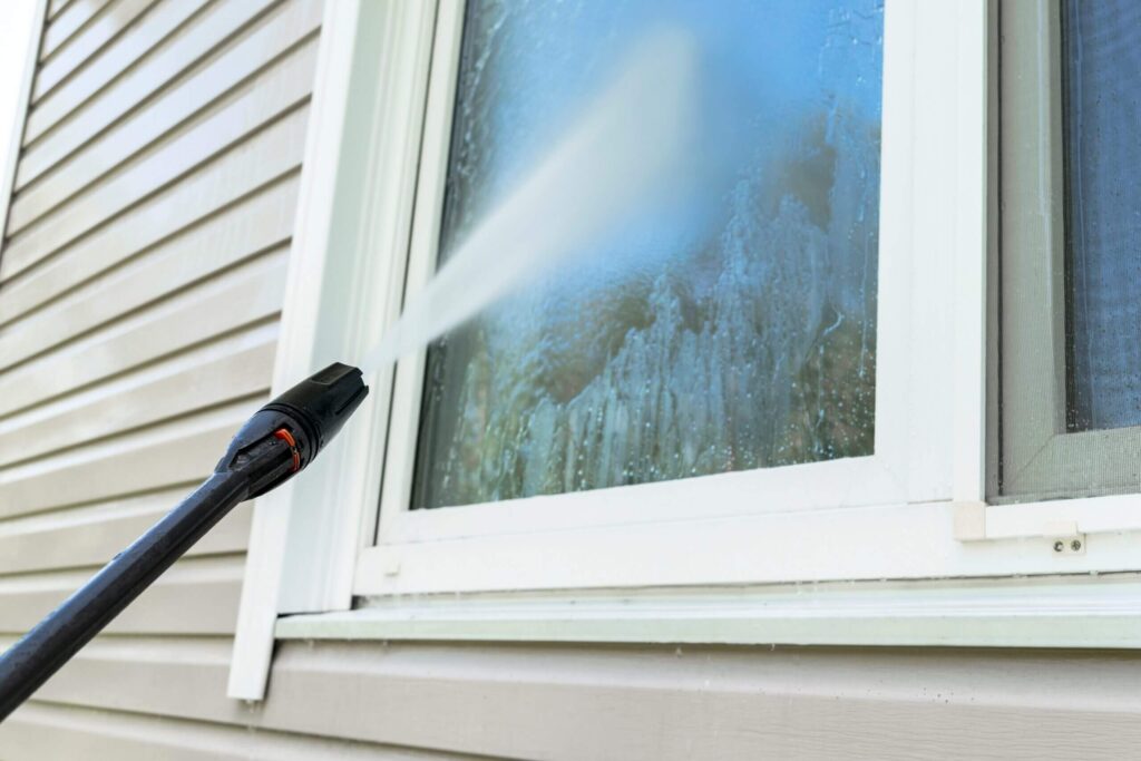 Close-up of a pressure washer spraying water on a residential window, showcasing the cleaning process for streak-free results.