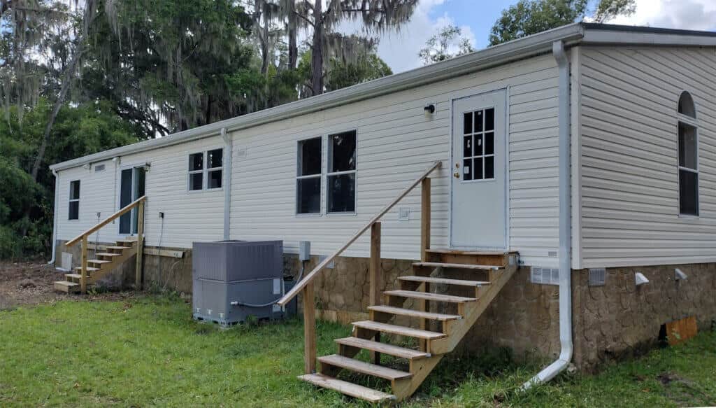 Exterior view of a clean white mobile home with horizontal vinyl siding, surrounded by greenery, showcasing well-maintained steps and a cooling unit, emphasizing the benefits of professional washing services by Starr's & Stripes PowerWash.