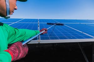 A worker using a long-handled brush to perform professional solar panel cleaning on a large commercial solar array in Fresno, CA.