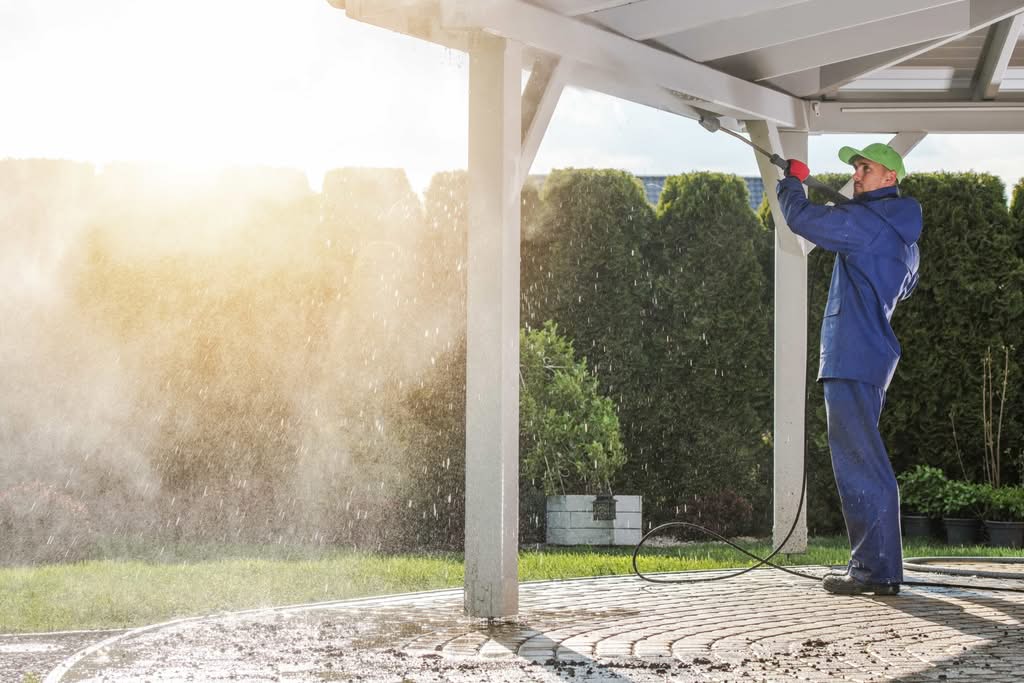 Prevent Costly Damage: Gutter Cleaning Power Washing (2026) 2 A professional cleaner in protective gear using a pressure washer to clean the exterior wooden structure of a suburban home in Atlanta, GA.