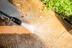 A close-up view of a pressure washing wand cleaning a dirty concrete driveway in Charlotte, NC, showing the contrast between the clean surface and the grime being removed.