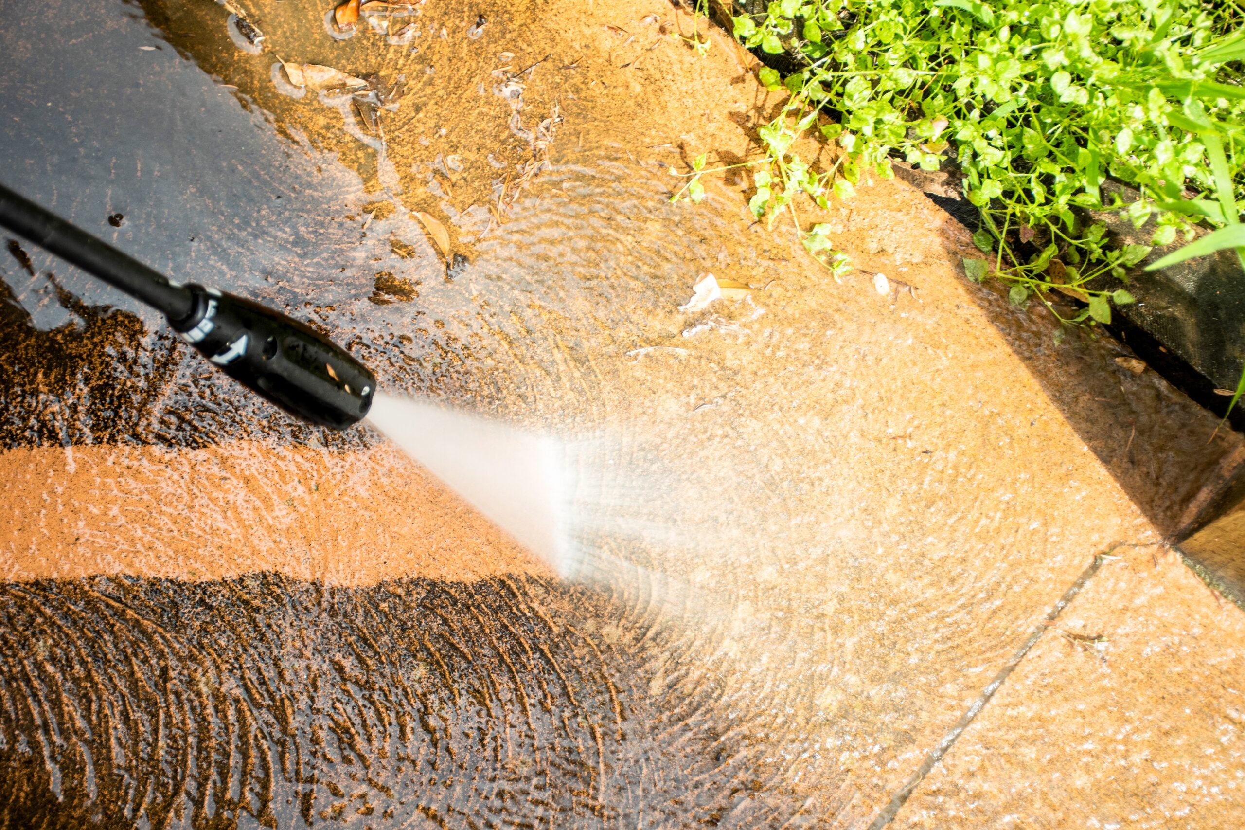 A close-up view of a pressure washing services wand cleaning a dirty concrete driveway in Charlotte, NC, showing the contrast between the clean surface and the grime being removed.