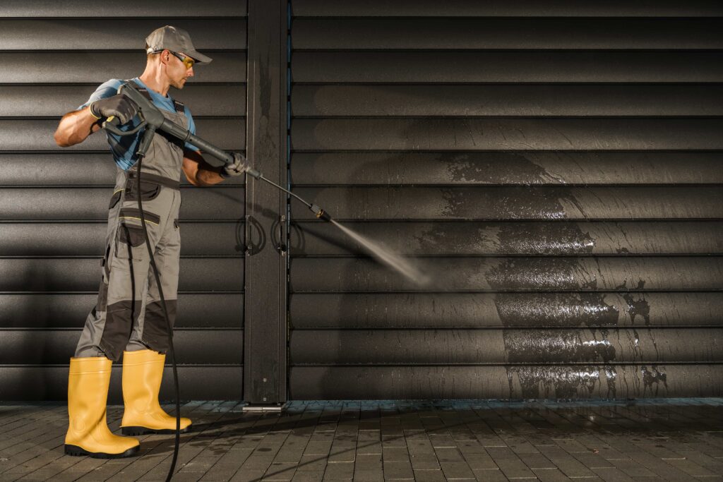 Ocala Commercial Cleaning: Facility Manager's Guide 2 A maintenance worker wearing protective gear uses a pressure washer to clean a dirty exterior metal wall in Austin, Texas.