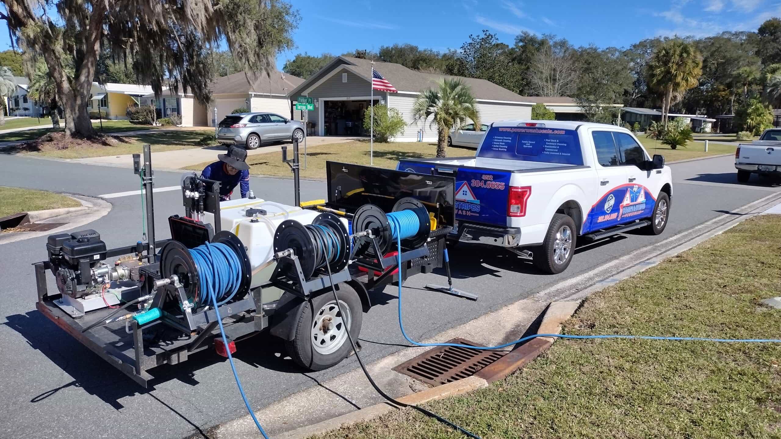 New Contact 7 A technician with Stars and Stripes Powerwash sets up a professional pressure washing trailer rig, complete with hose reels and a water tank, on a residential street in Ocala, FL.