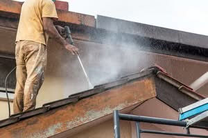A professional worker using a high-pressure water jet spray gun to clean a residential roof in Houston, TX, removing dirt and debris and gutter cleaning power washing.