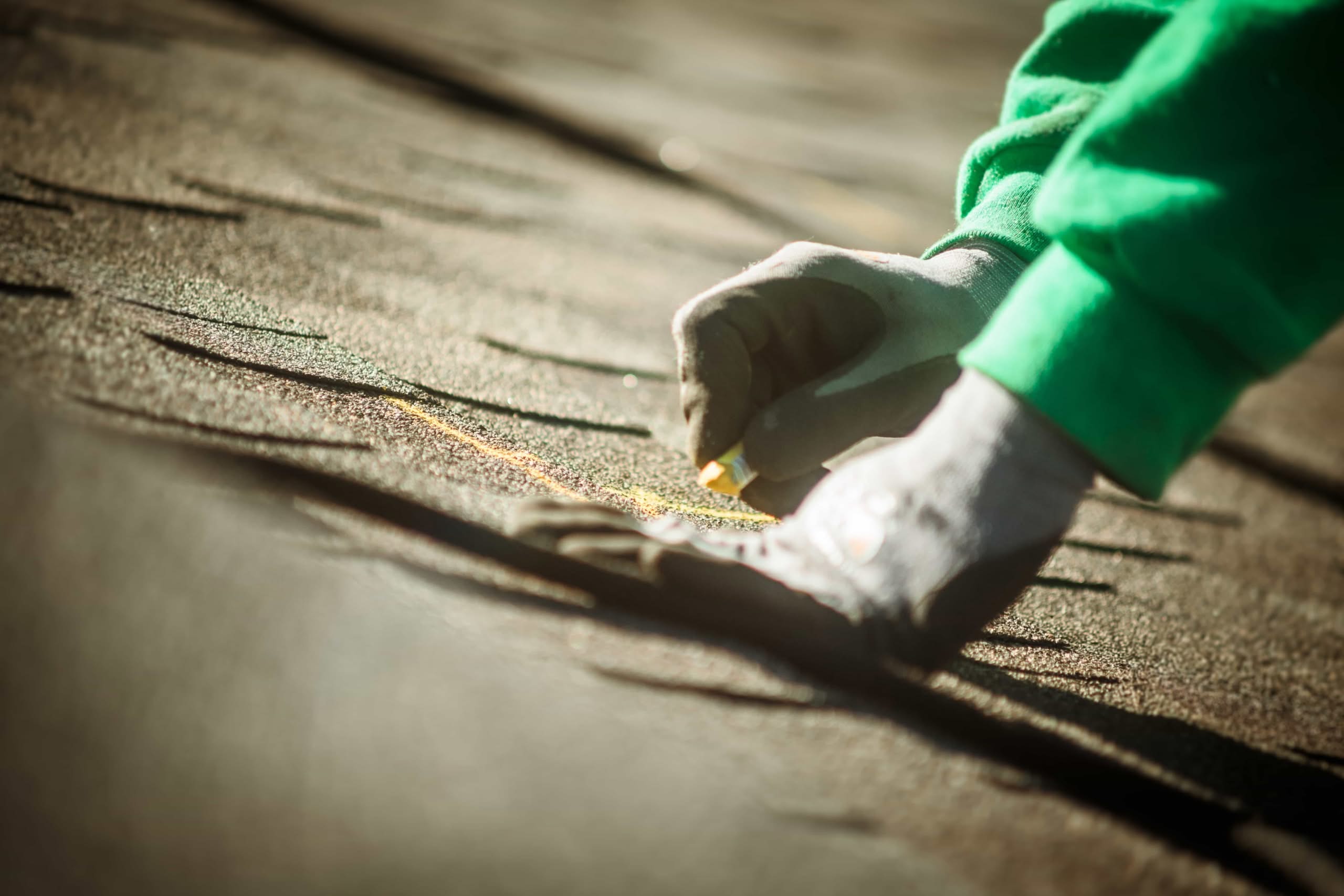 Asphalt Shingle Roof Warranty Traps: Save Your $10K Coverage 1 A close-up of a roofer's gloved hands using chalk to mark guidelines on dark asphalt shingles during a roof installation in Dallas, TX.